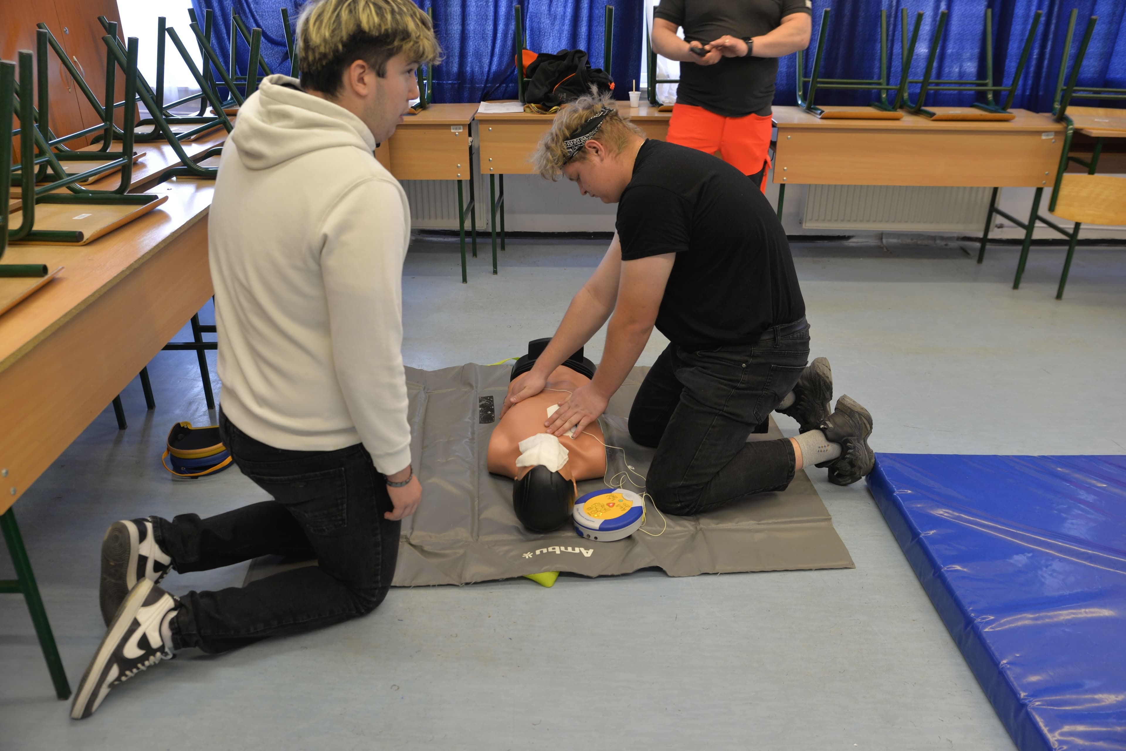 Students practicing CPR and AED skills with a training manikin in a classroom