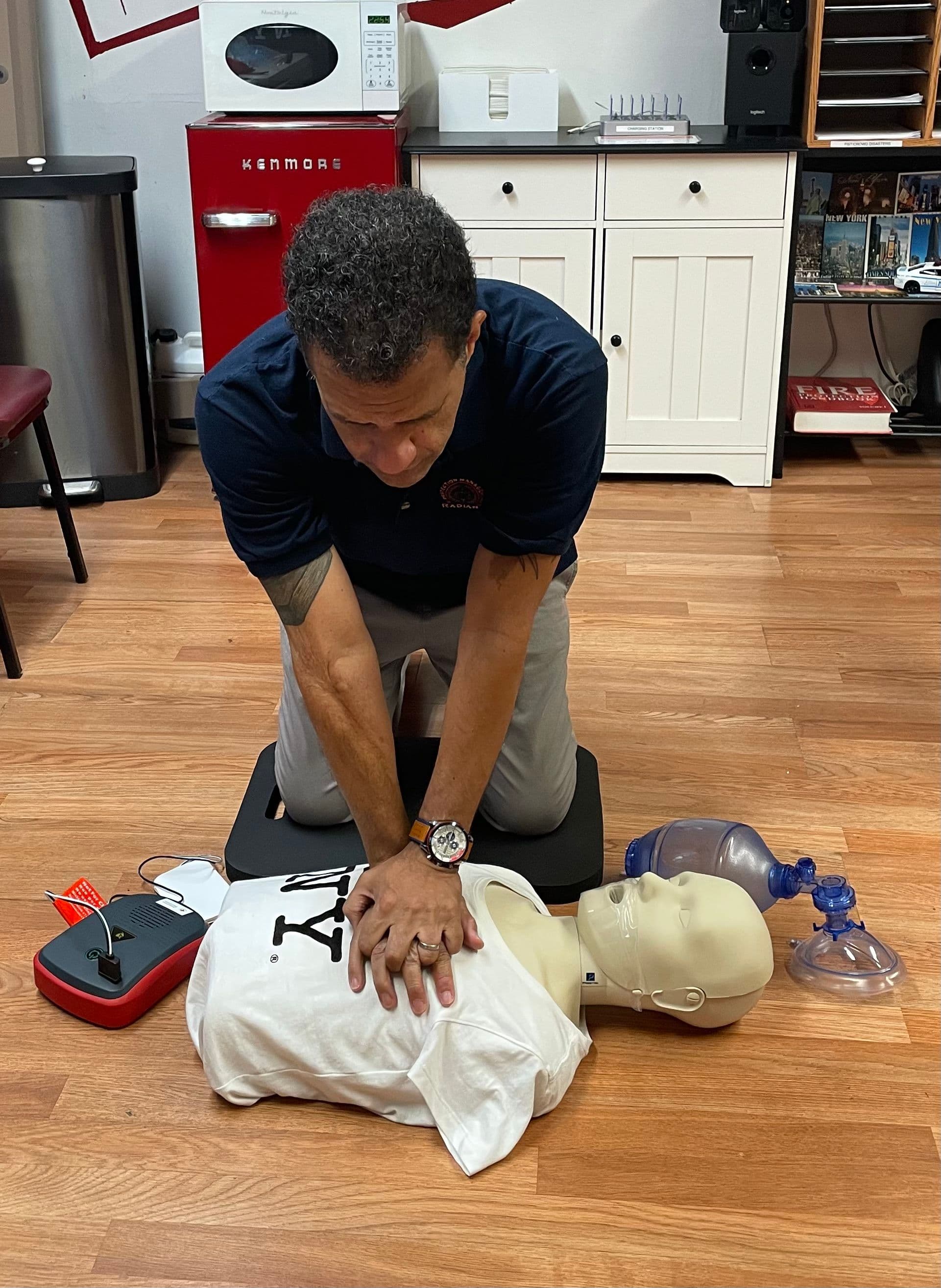Radiant instructor demonstrating CPR on a training manikin beside an AED trainer